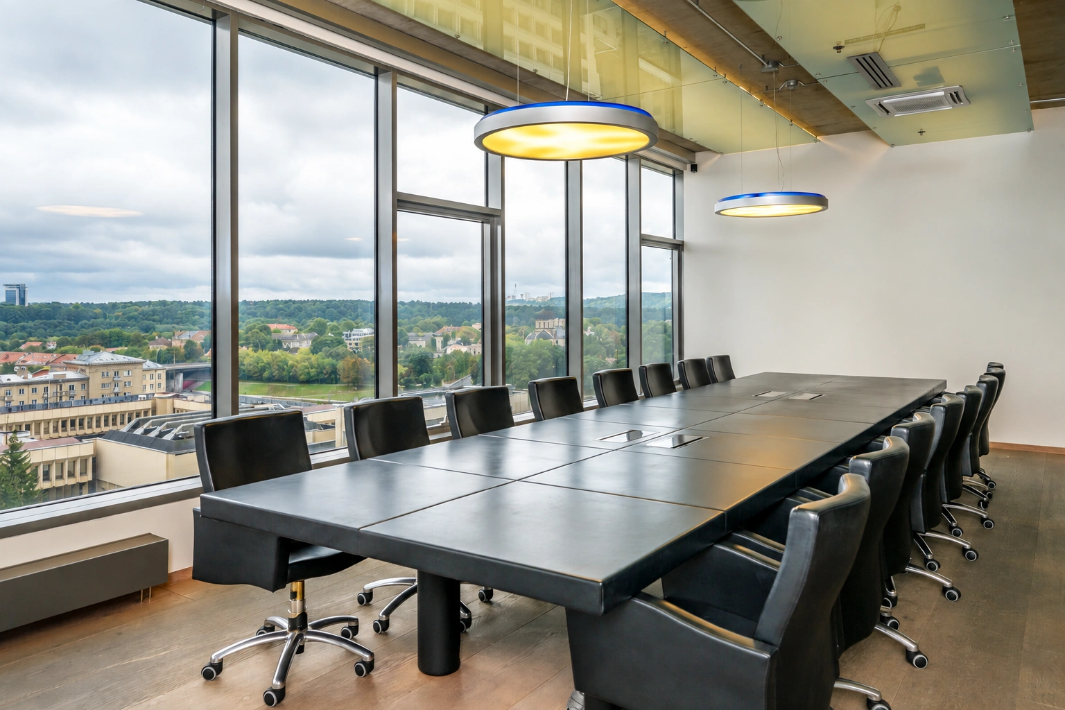 A meeting room with a long table, black office chairs, and large windows.