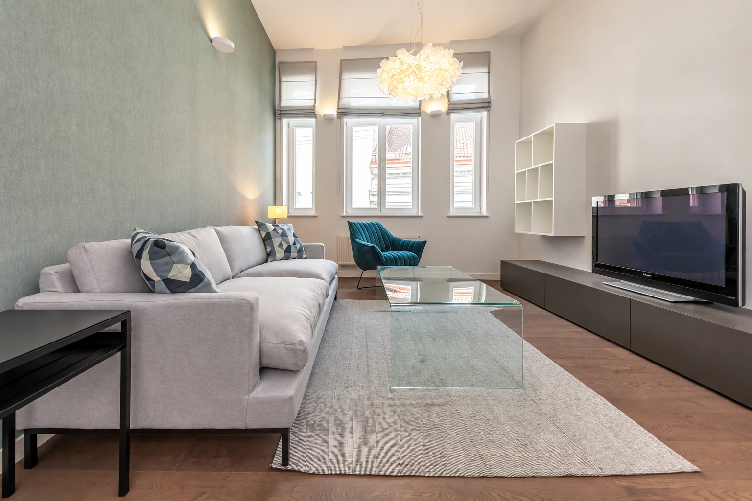 Svetainė su šviesia sofa ir televizoriumi ant ilgos žemos spintelės.