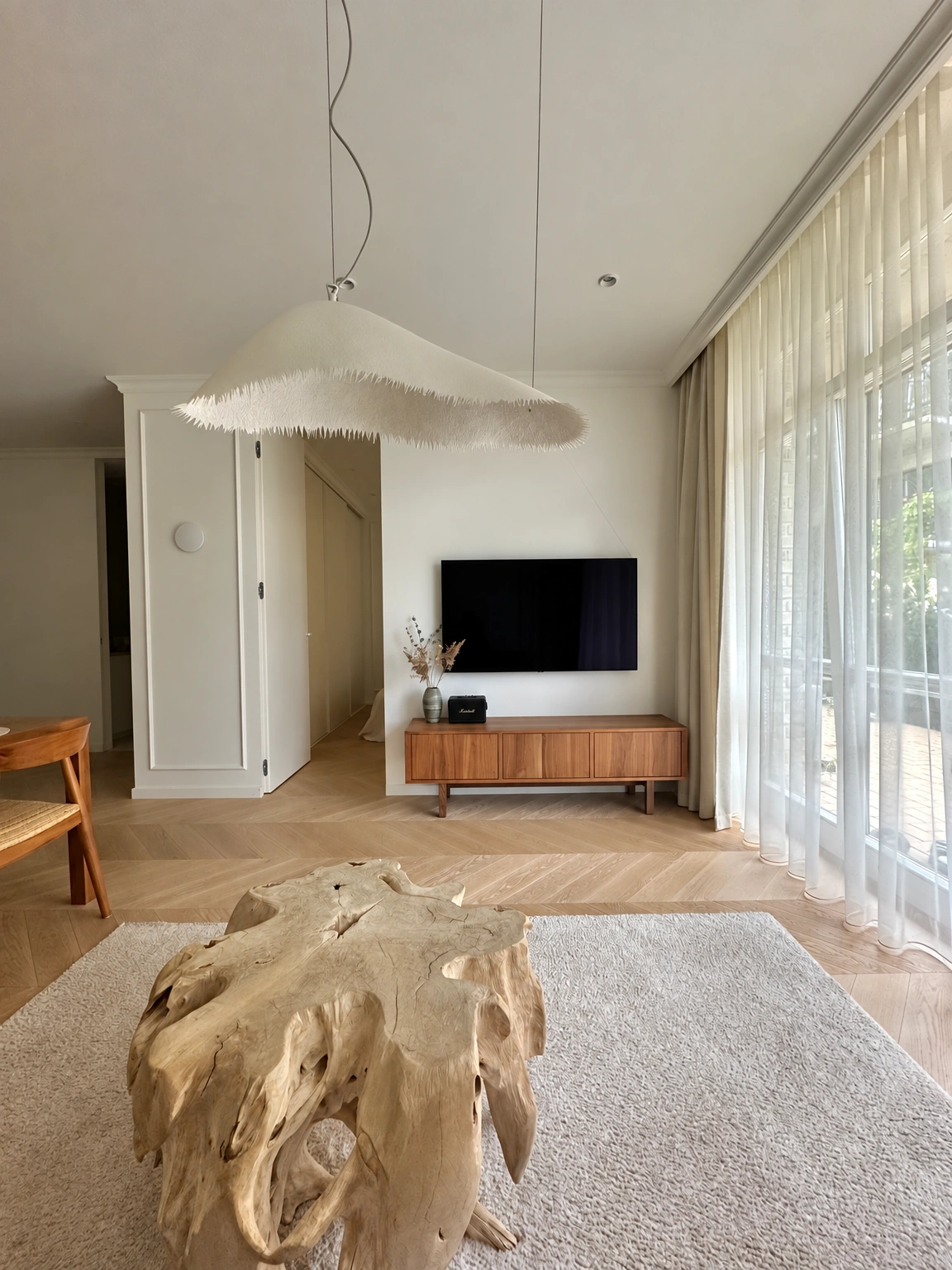 Im Wohnzimmer hängt ein Fernseher an der Wand, und transparente Vorhänge bedecken die großen Fenster.