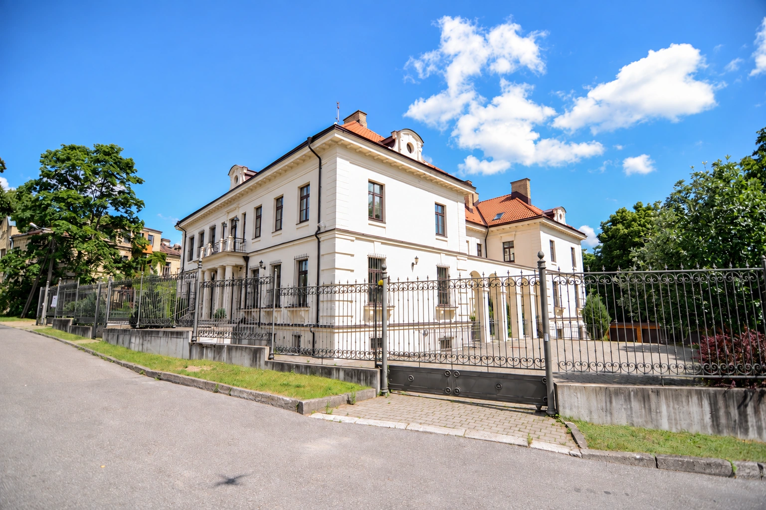 A light-colored two-story building with a red roof and a fence by the street.