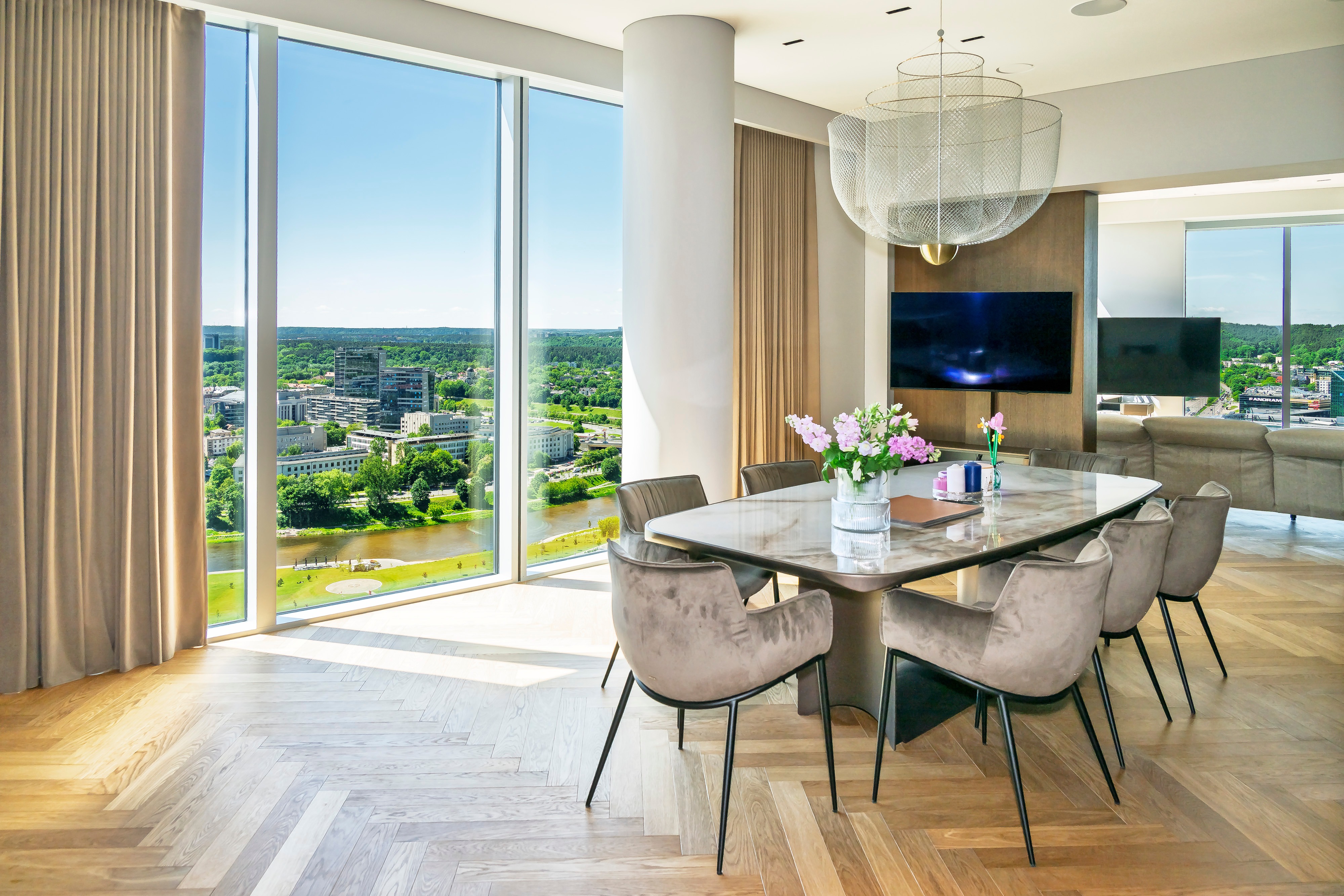 Dining area with a table, chairs and large windows through which greenery can be seen.