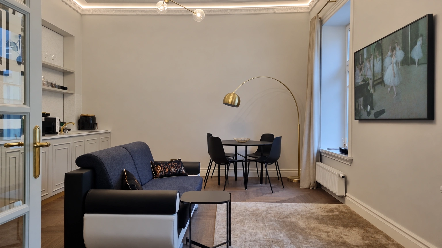 Svetainėje stovi tamsi sofa ir apvalus valgomojo stalas su kėdėmis.