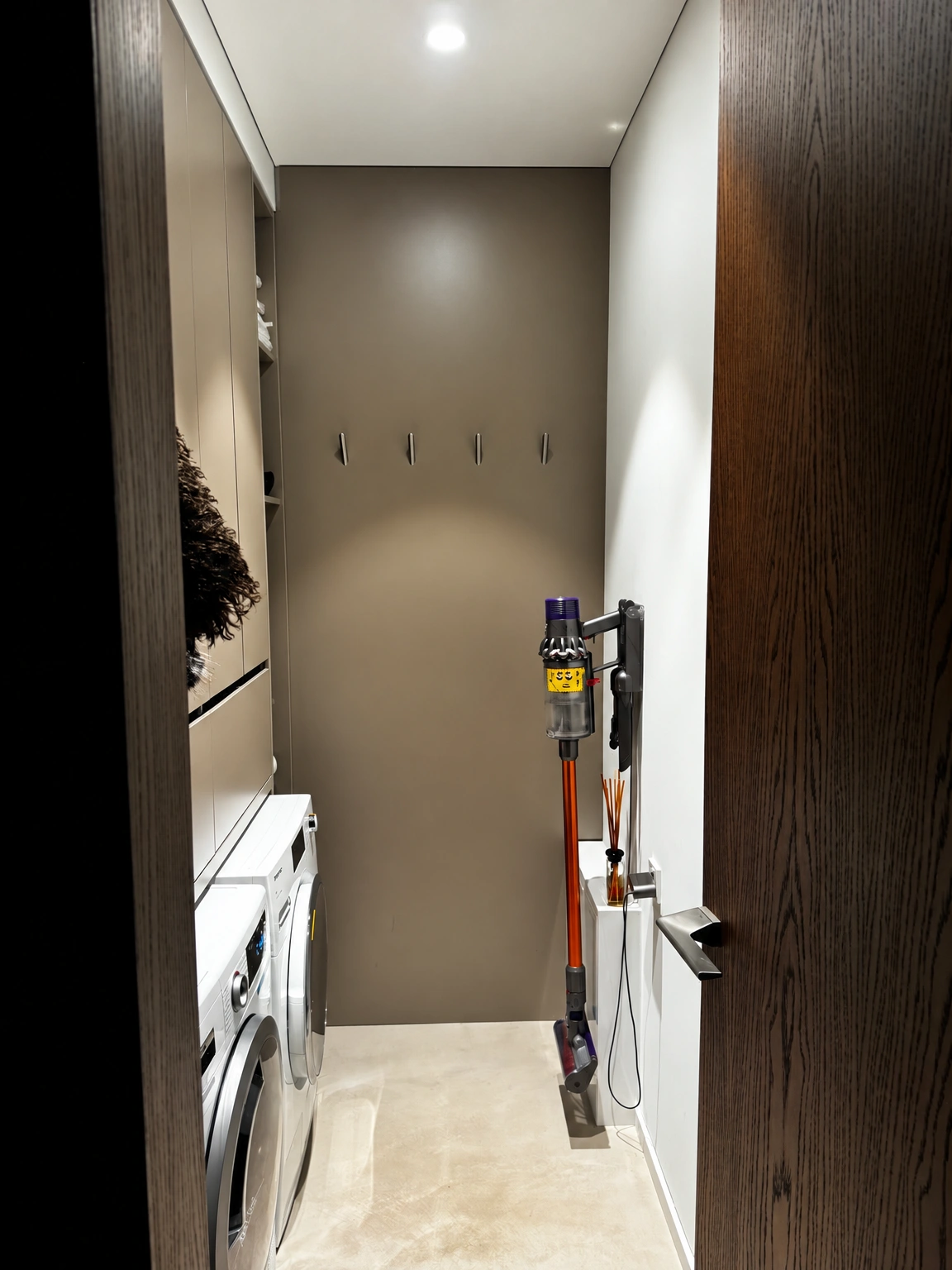 A narrow room with a washing machine and a vacuum cleaner mounted on the wall.