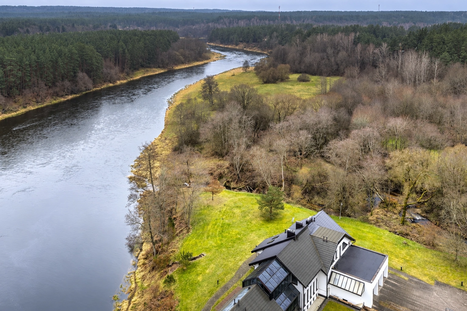 Ein Haus an einem sich schlängelnden Fluss, umgeben von Rasen und Bäumen.