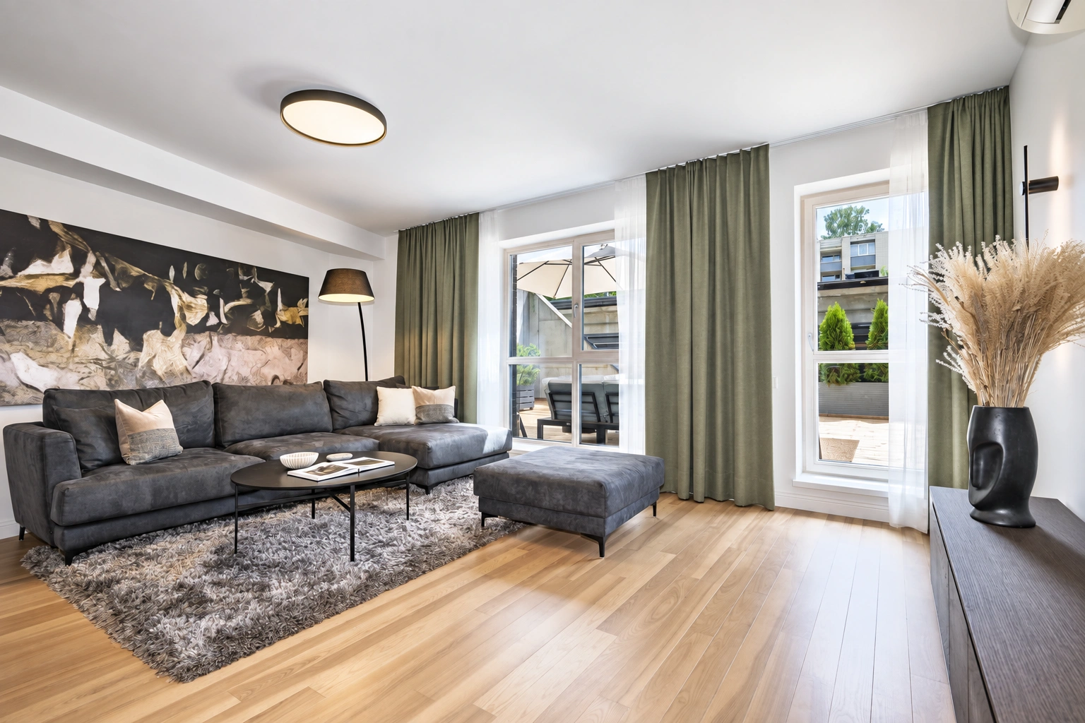 Im Wohnzimmer steht ein dunkles Sofa, und an den hohen Fenstern hängen grüne Vorhänge.