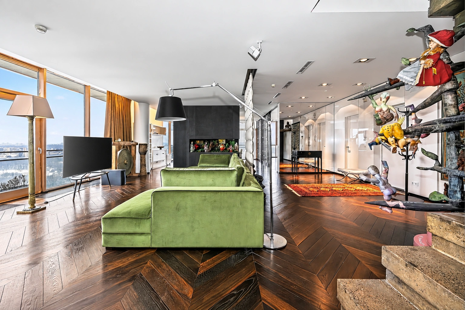 Wohnzimmer mit einem grünen Sofa und großen Fenstern auf der linken Seite.