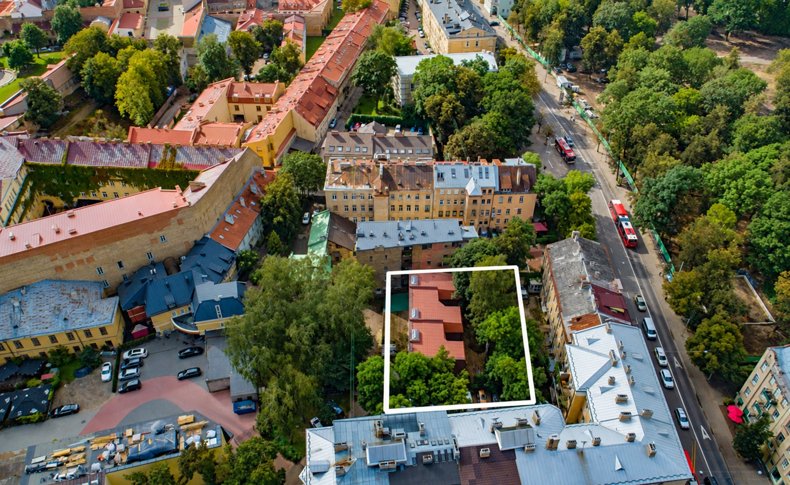 Von oben sind Gebäude, ein mit Bäumen bewachsener Hof und eine angrenzende Straße mit Autos zu sehen.
