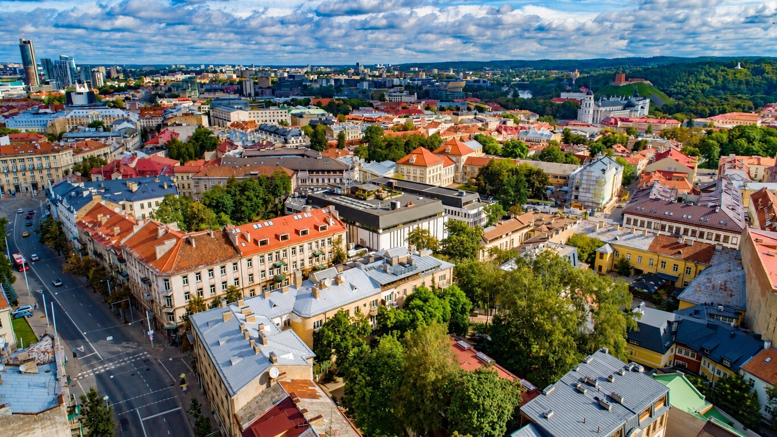 Iš aukštai matyti miesto pastatai raudonais stogais, gatvės ir medžiai.