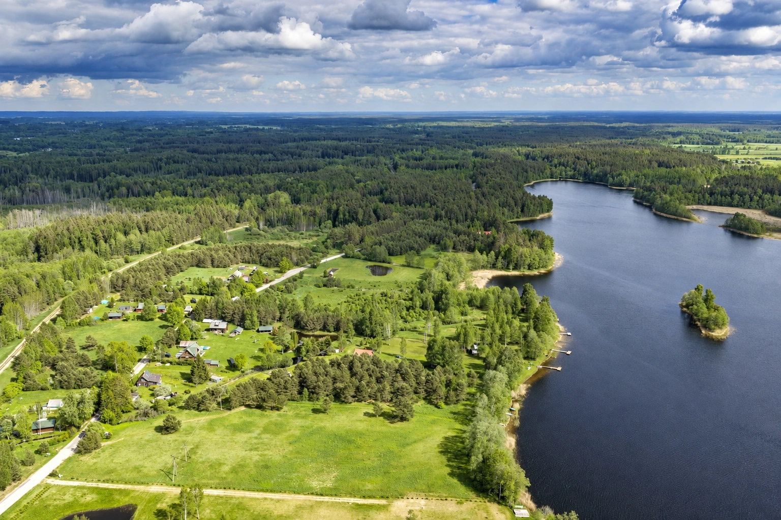 A lake with a small island is seen from the air, with meadows and forests stretching along the shore.