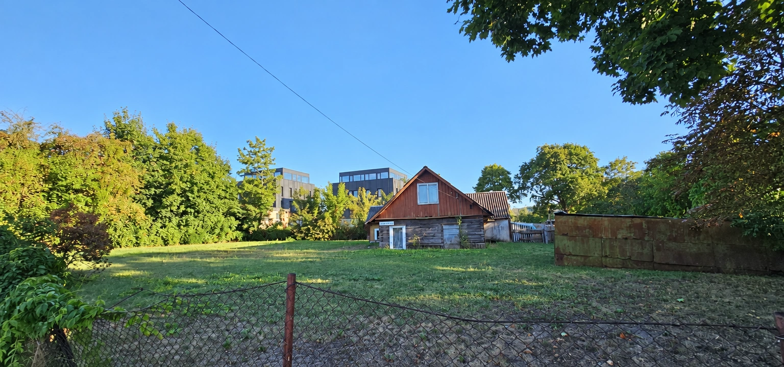 A grassy plot with a house, a fence, and trees growing around it.