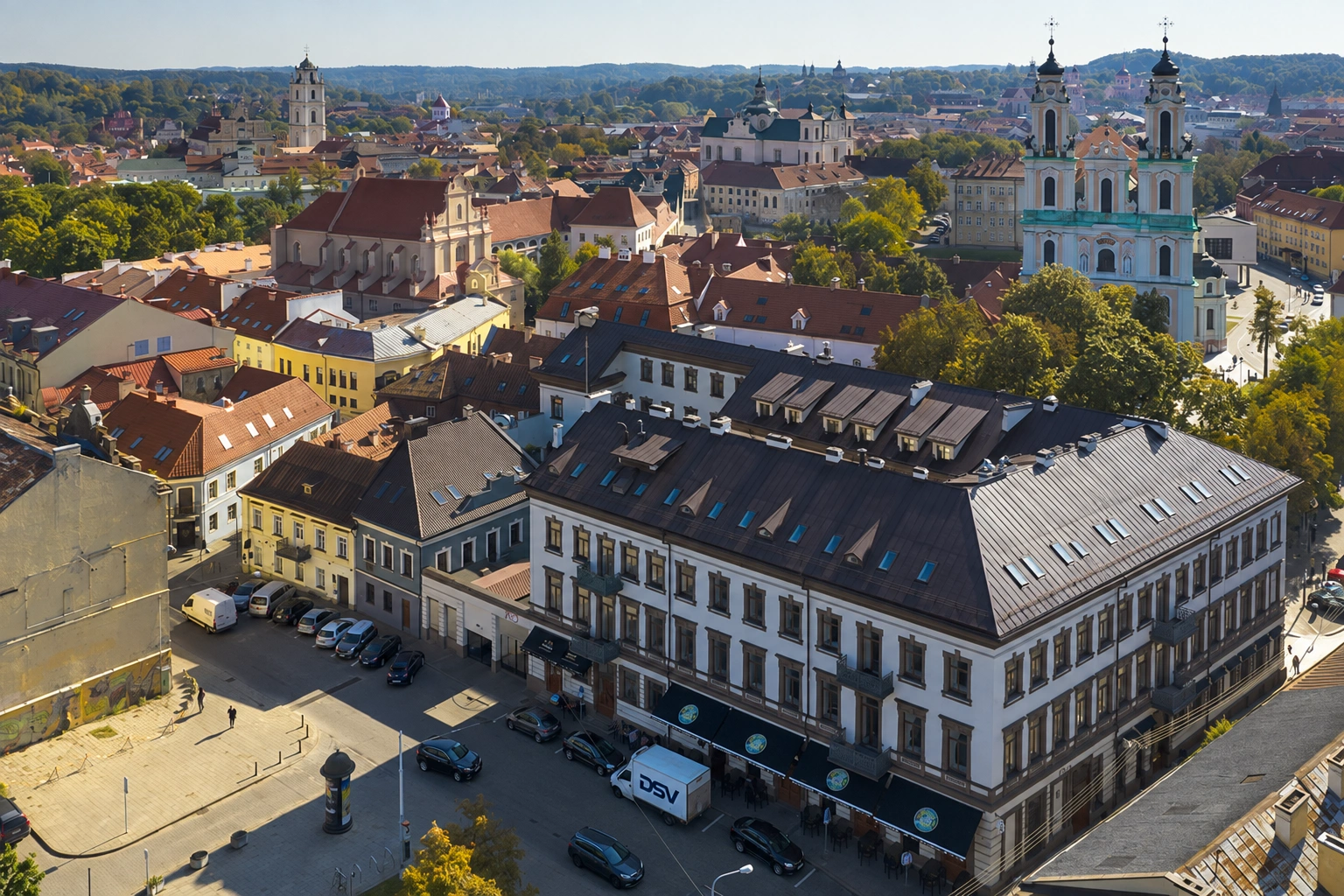 View of the city from above: a multi-storey corner building is visible in the foreground, with church towers in the distance.