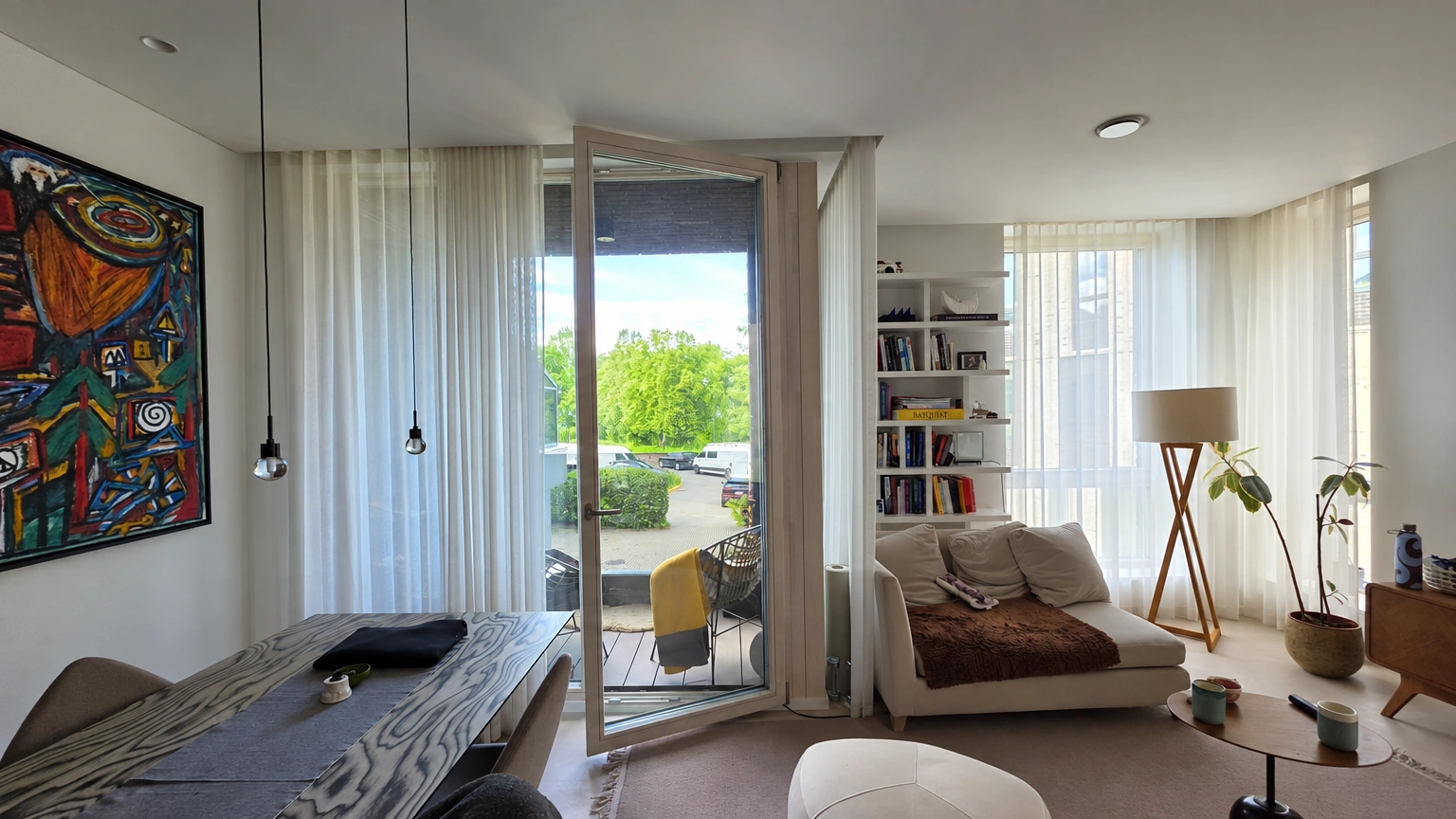 Living room with large windows, a brown armchair and a dining table.