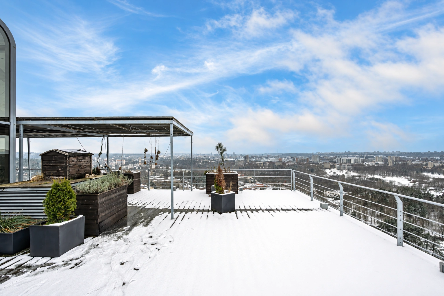 Eine schneebedeckte Dachterrasse mit Pflanzentöpfen und Geländern.