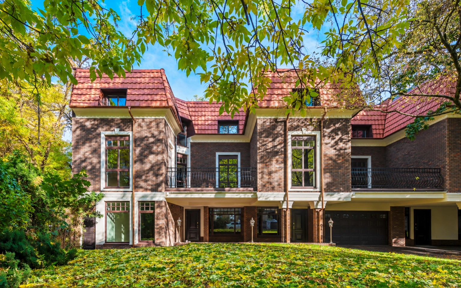 Ein Haus mit einem roten Dach und großen Fenstern, vor dem sich eine Rasenfläche erstreckt.