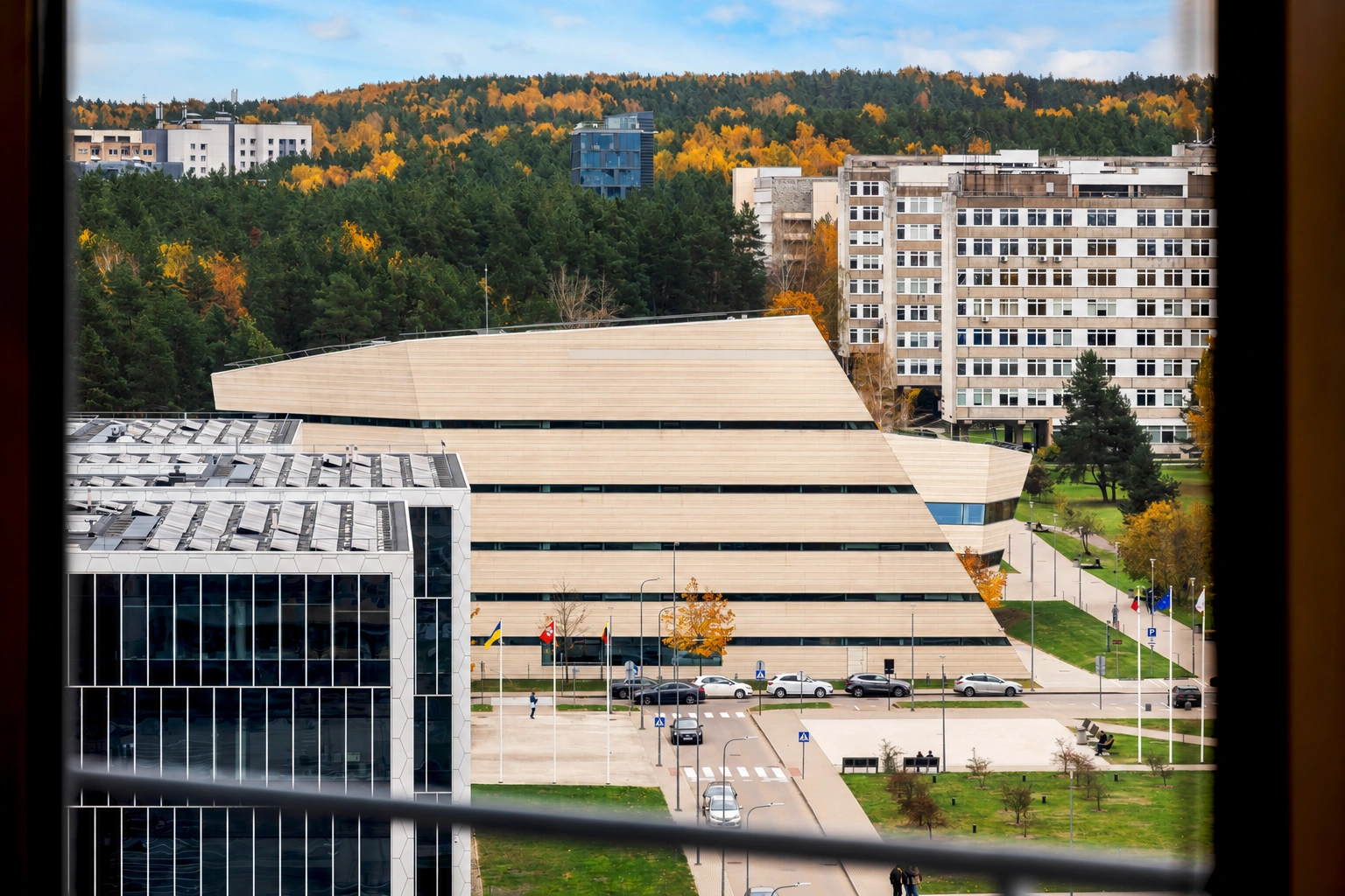 Durch das Fenster sind die umliegenden Gebäude, ein Parkplatz und sich herbstlich verfärbende Bäume zu sehen.