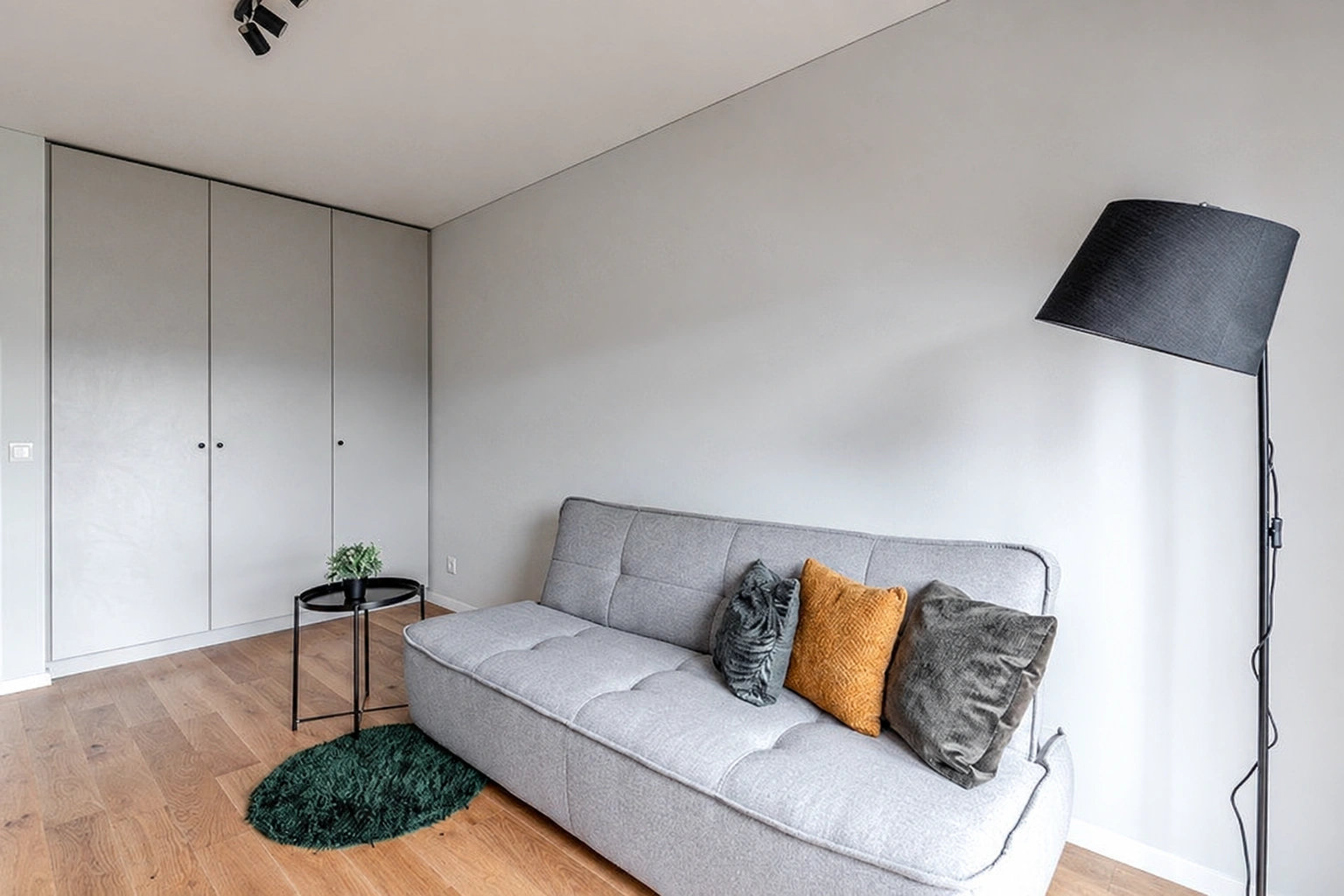 Eine Ecke des Wohnzimmers mit einem grauen Sofa, einem Einbauschrank und einer schwarzen Stehlampe.