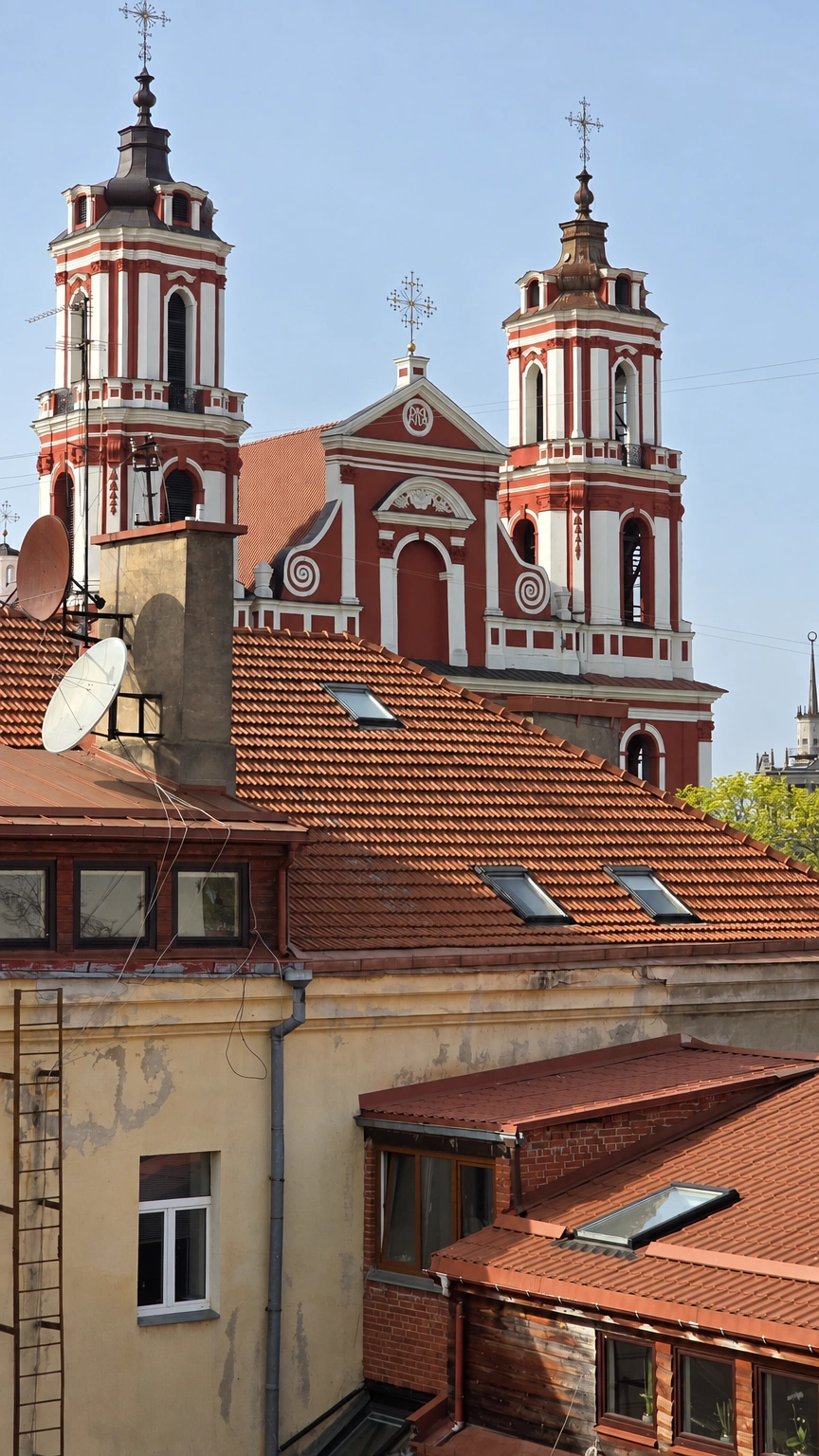 Hinter den Schrägdächern der Gebäude sind die Fassade einer Kirche und zwei Türme mit Kreuzen zu sehen.