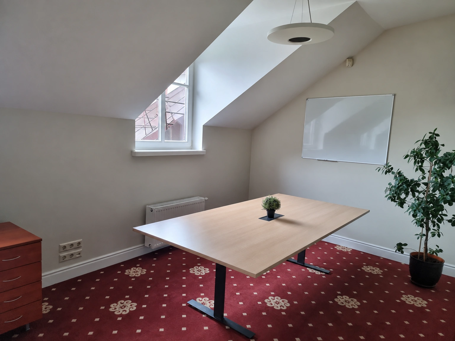 In a room with a sloping ceiling, there is a table, and a whiteboard hangs on the wall.