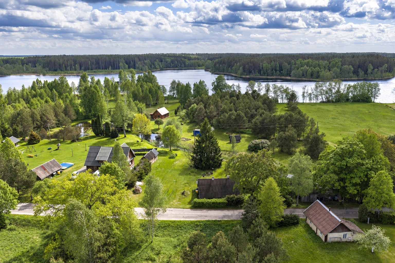 From above, several buildings can be seen among trees and meadows, with a lake stretching out in the distance.