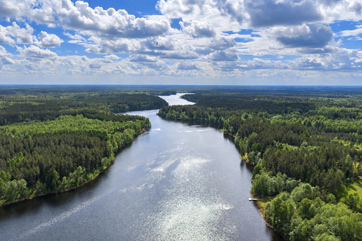From above, a wide river, wooded banks and a cloudy sky can be seen.