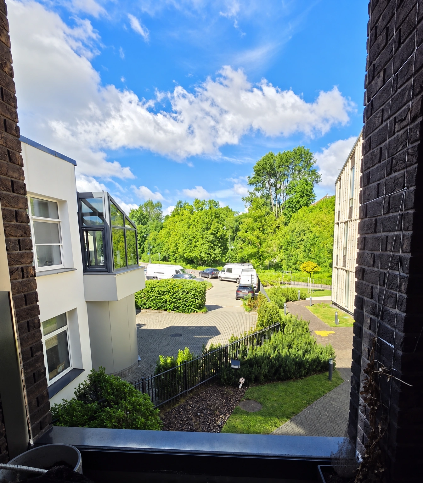 A courtyard with parked cars and green trees is visible through the window.