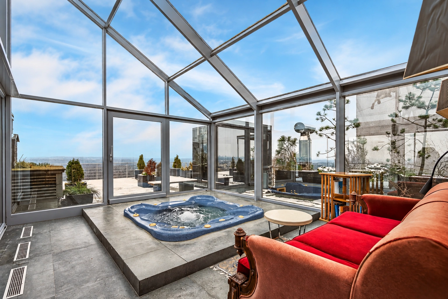 Auf der verglasten Terrasse ist ein Whirlpool installiert, daneben steht ein Sofa mit roten Kissen.