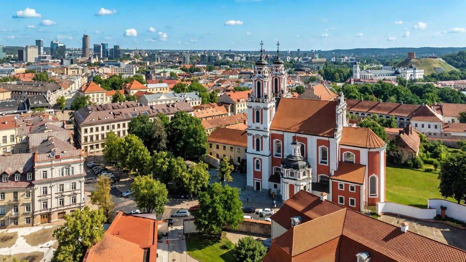 City panorama with church towers, red roofs of surrounding buildings, and trees.