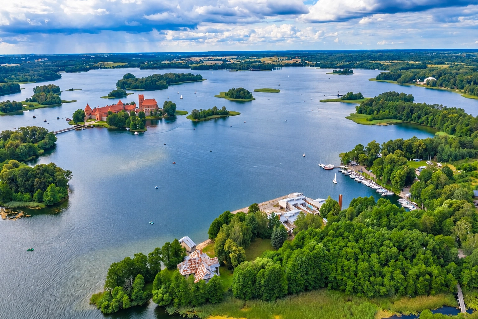 Ežero panorama su medžiais apaugusiomis salomis ir vienoje jų stovinčia pilimi raudonais stogais.