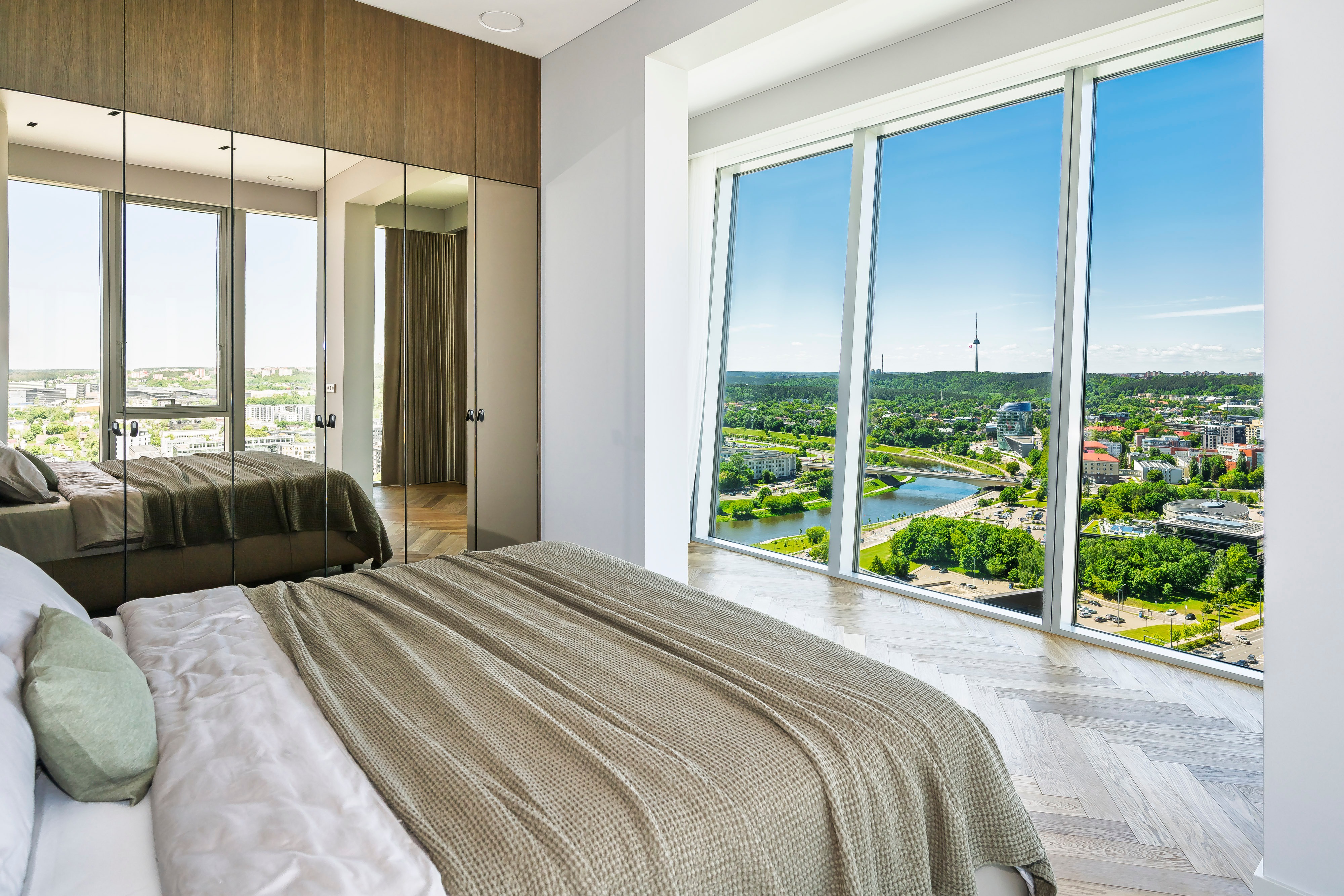 Bedroom with a double bed, a mirrored wardrobe and large windows through which the city can be seen.