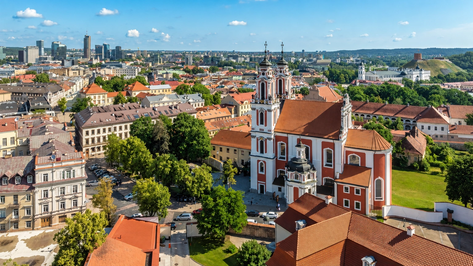 Stadtpanorama mit den Türmen einer Kirche und den roten Dächern der umliegenden Gebäude.