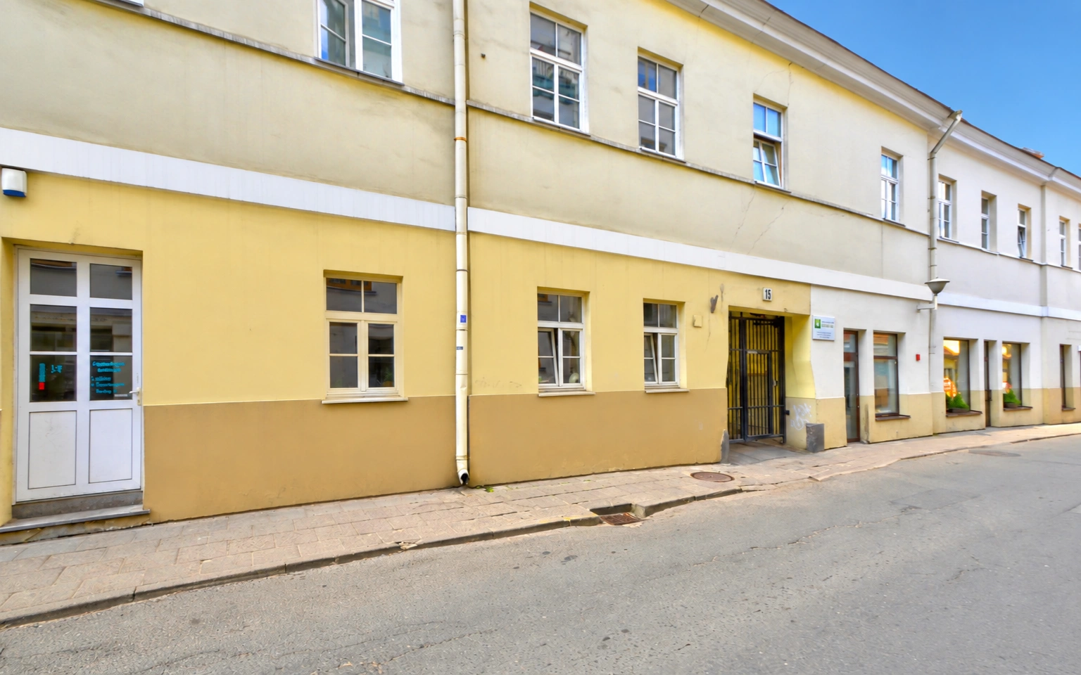 Die Fassade eines gelben zweistöckigen Gebäudes mit Fenstern und Türen neben einem Gehweg und einer Straße.