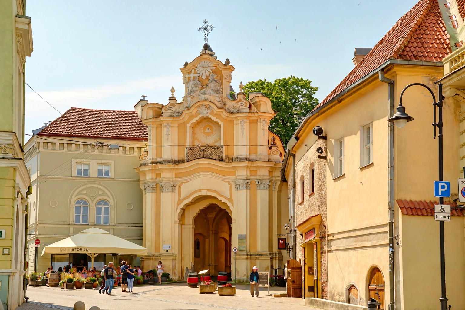 Building façade with an arched entrance; nearby are outdoor café umbrellas and passersby.
