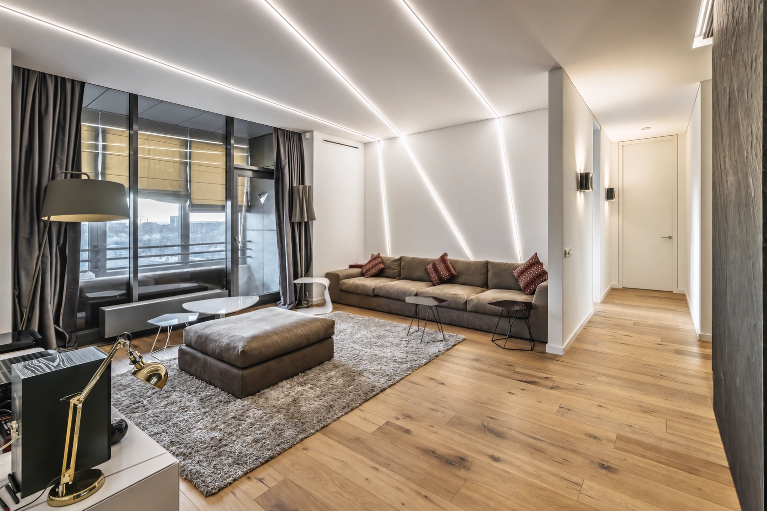 Living room with a sofa and a pouf, large windows, and lighting strips in the ceiling.