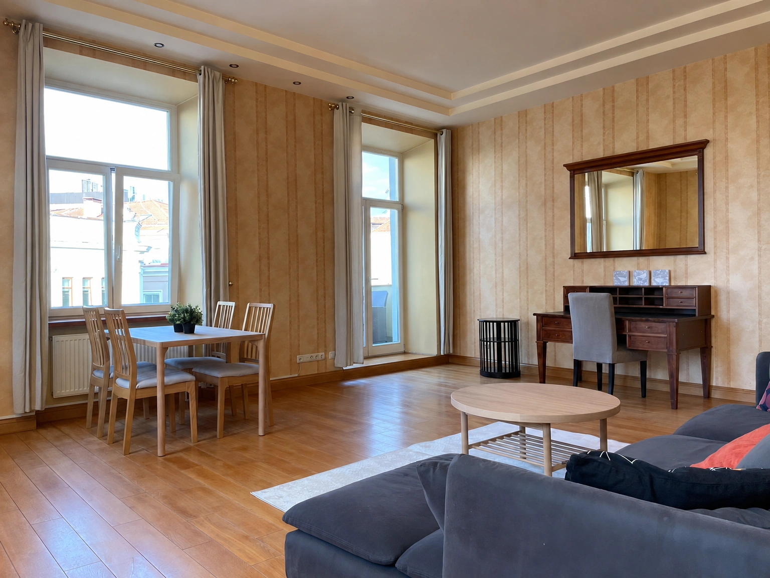 Wohnzimmer mit einem dunklen Sofa und einem Esstisch an einem großen Fenster.