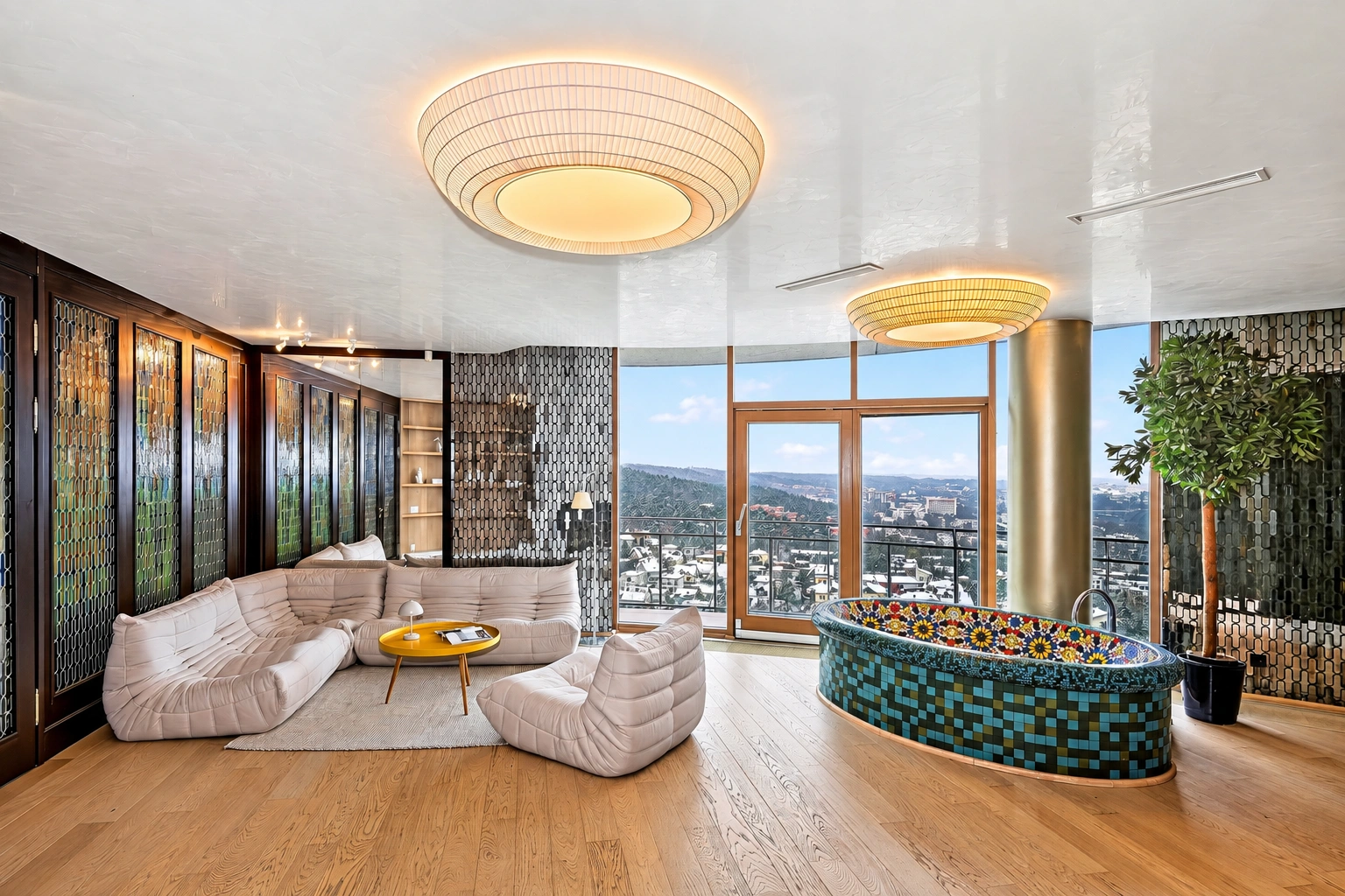 Im Ruhebereich stehen helle Sofas und ein kleiner runder Tisch; durch die großen Fenster ist ein Stadtpanorama zu sehen.