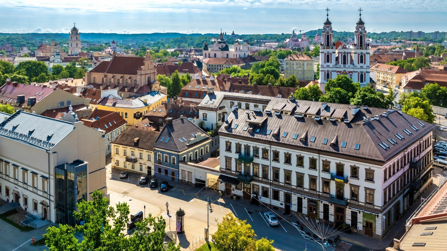 In the city centre, multi-storey buildings, a street and the towers of a church rising above the rooftops are visible.