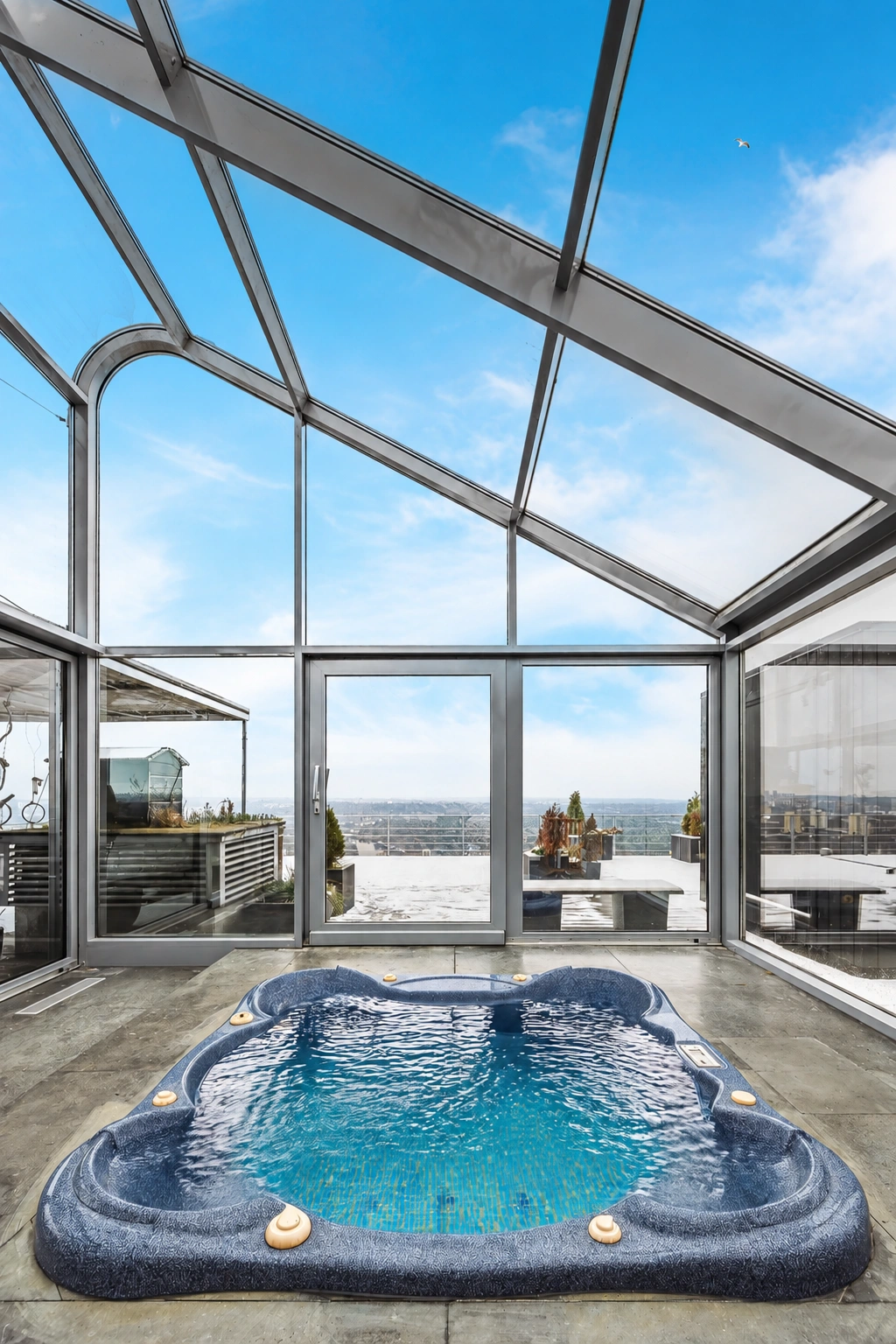 Auf einer verglasten Terrasse unter einem schrägen Dach steht ein mit Wasser gefüllter Whirlpool.