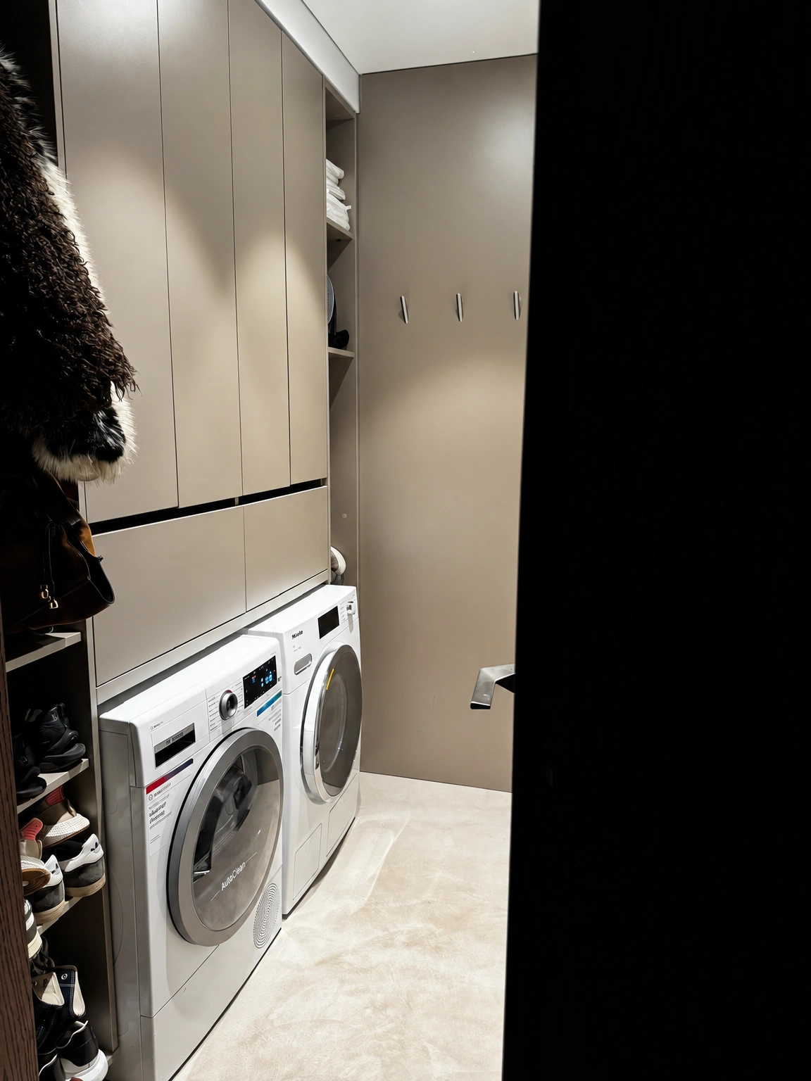 In a narrow room, a washing machine and a dryer stand side by side, with cabinets installed above them.