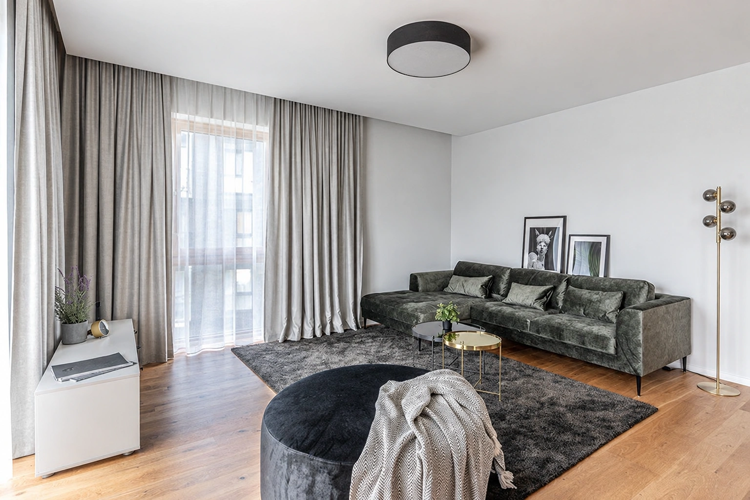Wohnzimmer mit einem grünen Sofa und großen Fenstern, die mit langen Vorhängen verhängt sind.