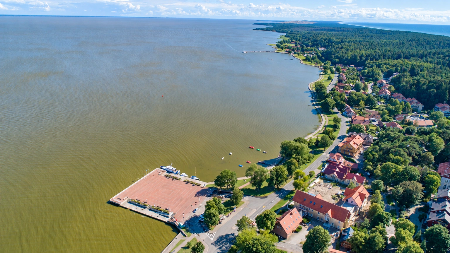 Iš viršaus matyti vandens telkinys, pakrantėje išsidėstę namai ir medžiai.