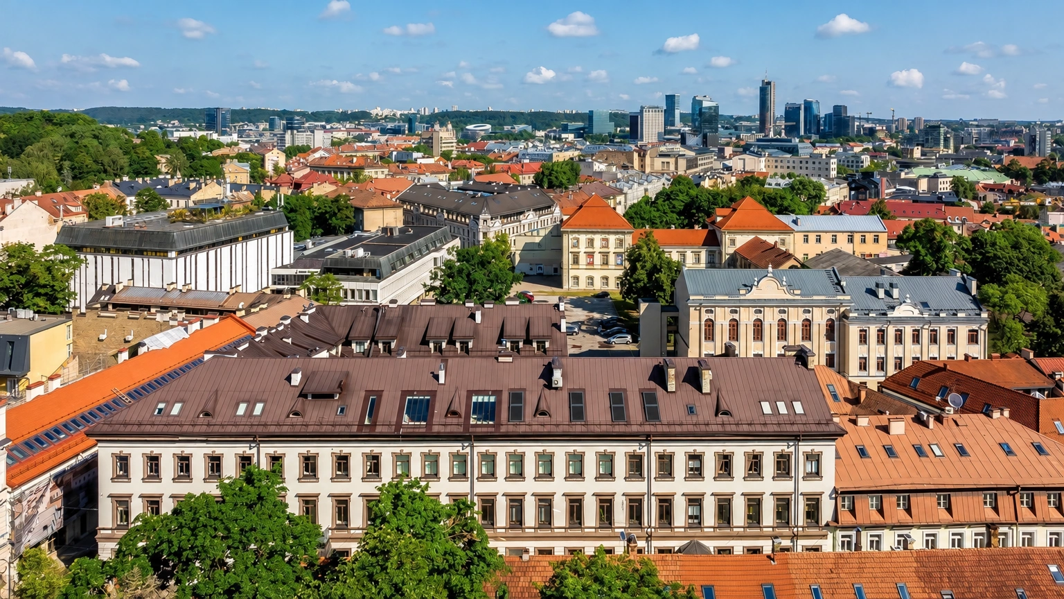 City panorama with red building roofs and high-rise buildings visible in the distance.
