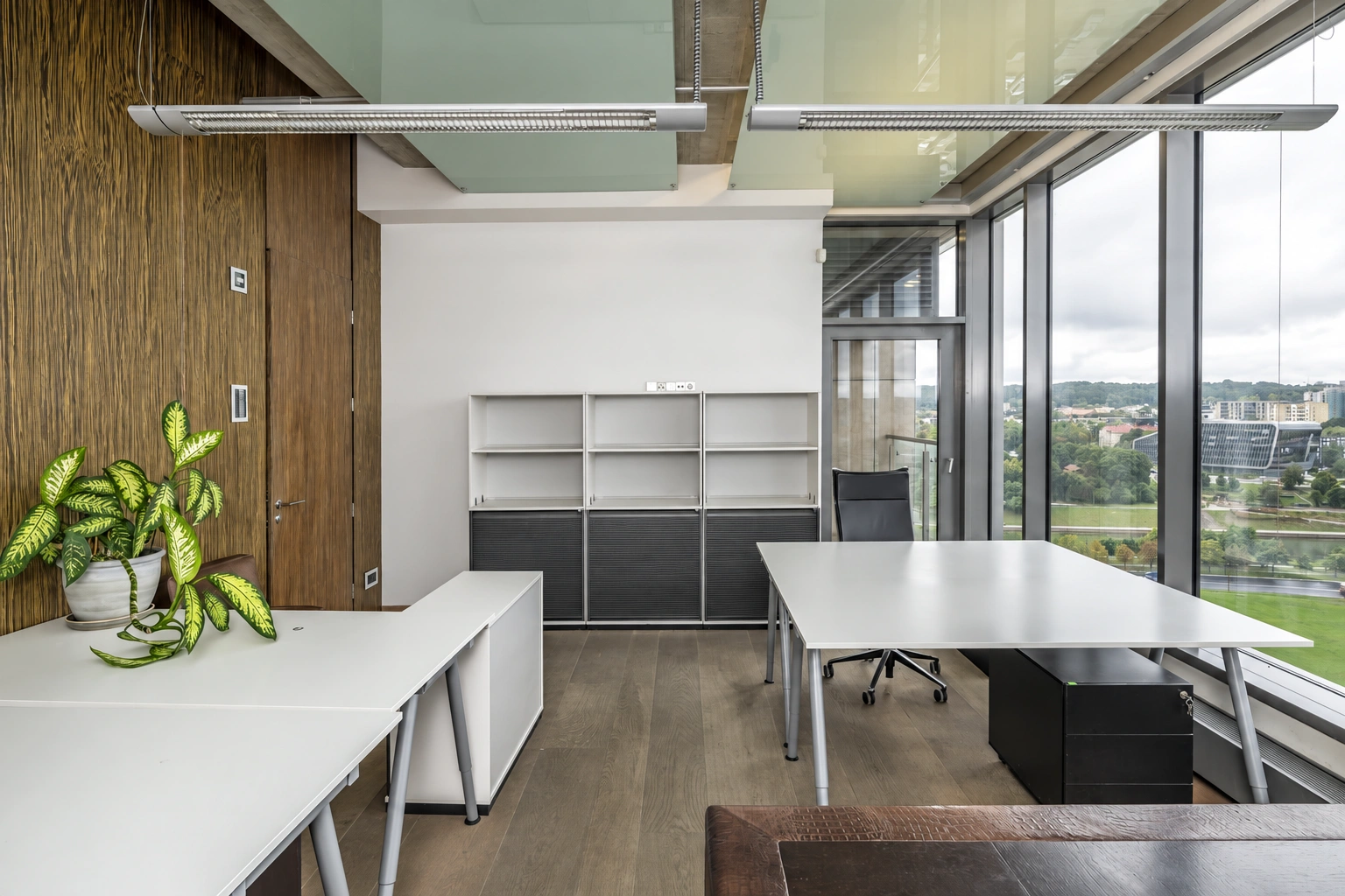 A workspace with white tables and large windows extending down to the floor.