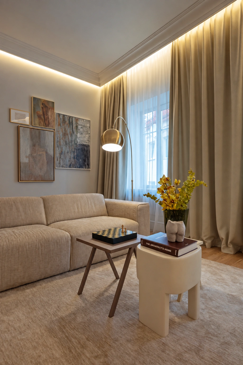 In the living room, a light-colored sofa, pictures on the wall and a window with long curtains can be seen.