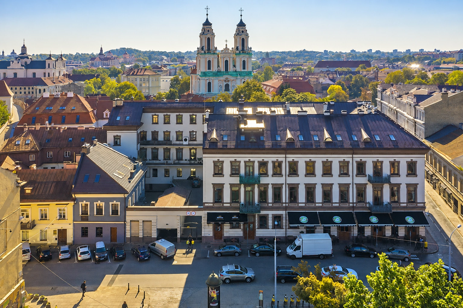 Panoramic view of the old town with cars parked in the square and two towers of a church visible in the distance.