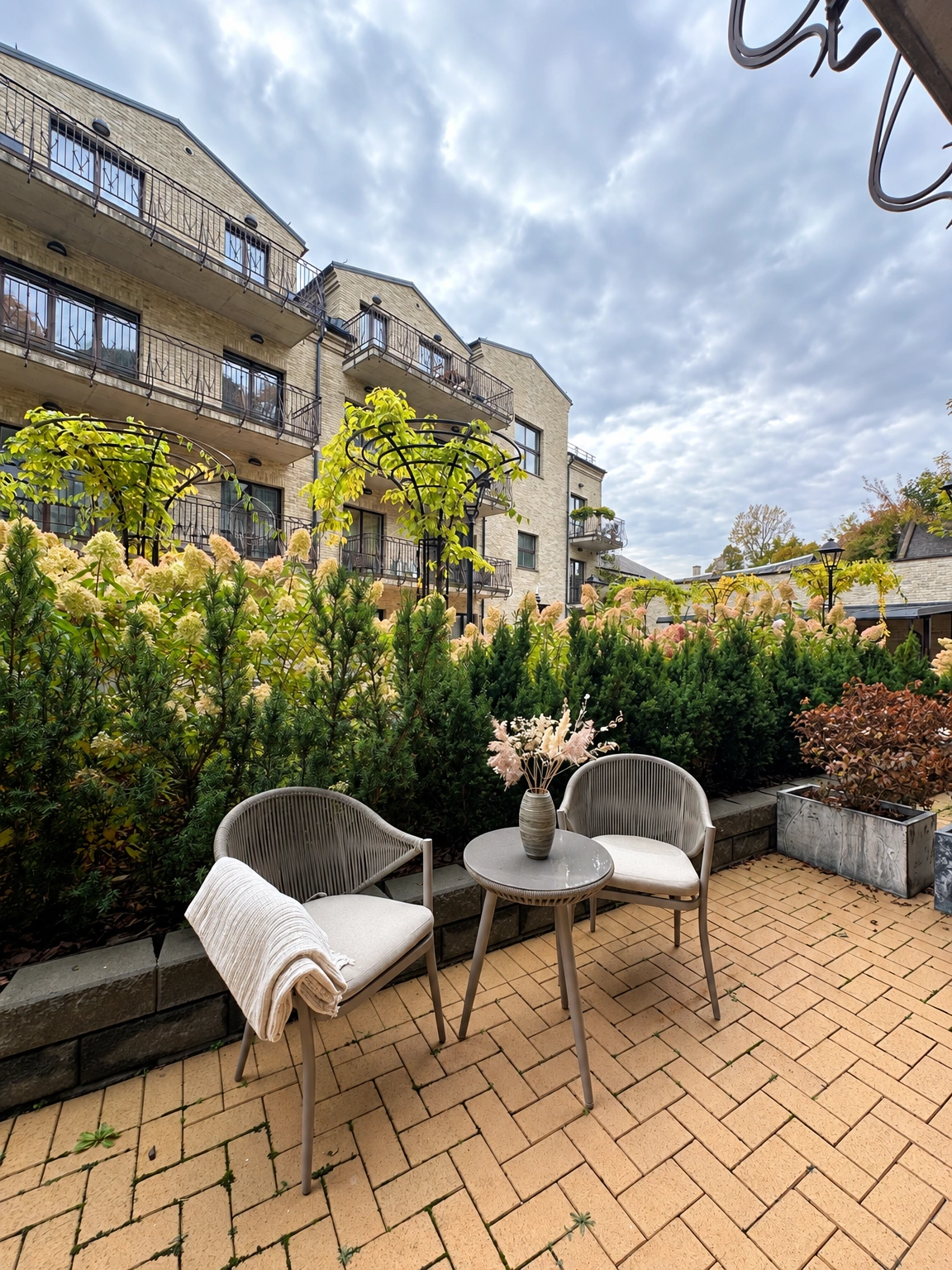Auf der Terrasse stehen neben der Hecke zwei Stühle und ein kleiner runder Tisch.