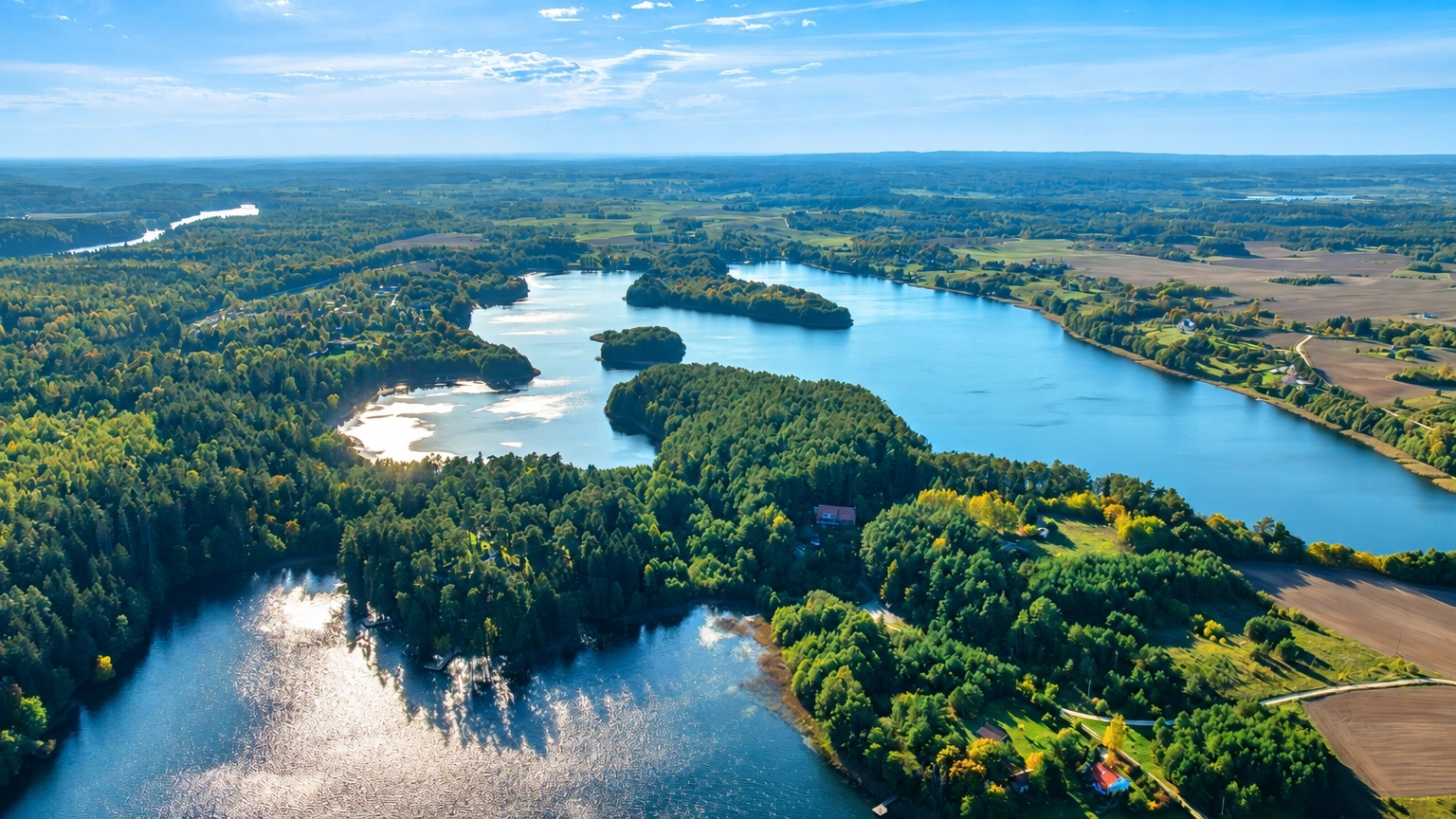 Aus der Luft ist ein See mit bewaldeten Ufern und sich daneben erstreckenden Feldern zu sehen.