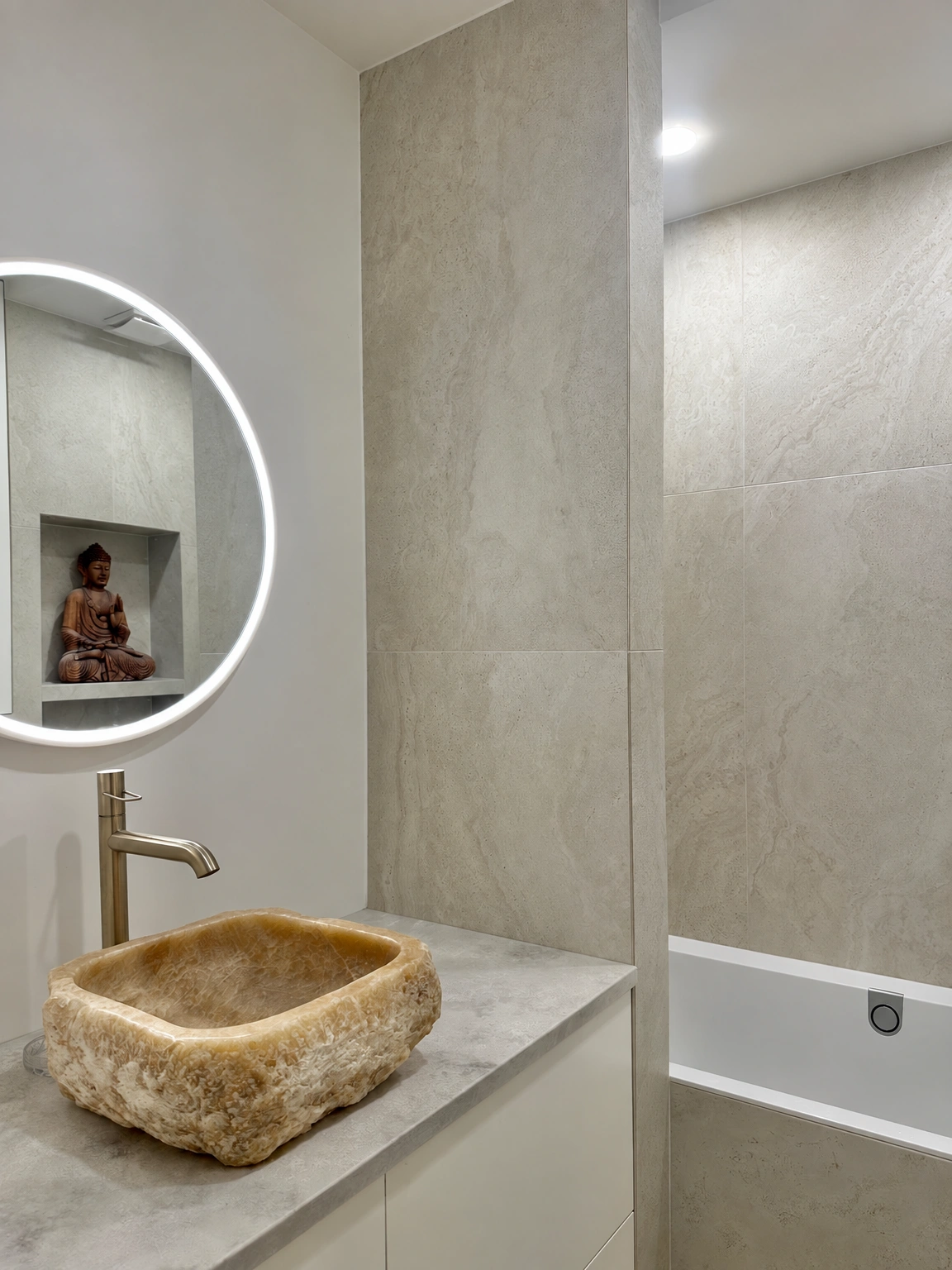 Badezimmer mit einem Waschbecken auf der Arbeitsplatte und einem beleuchteten runden Spiegel.