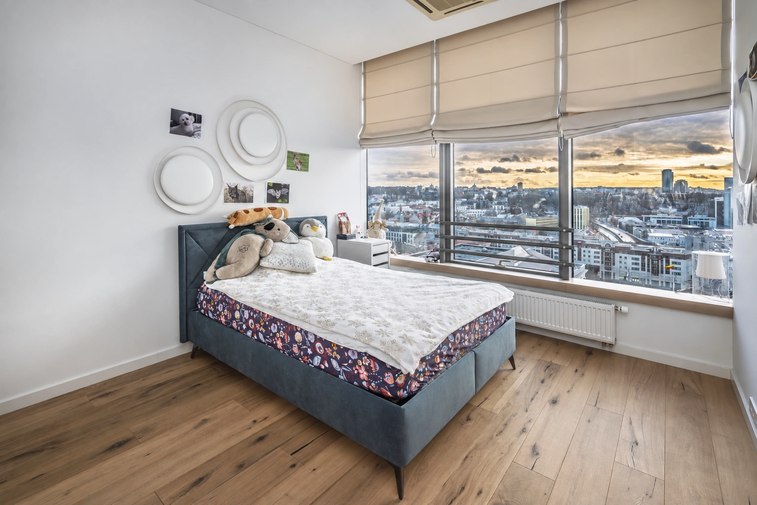 A bedroom with a double bed and large windows through which a panoramic view of the city can be seen.