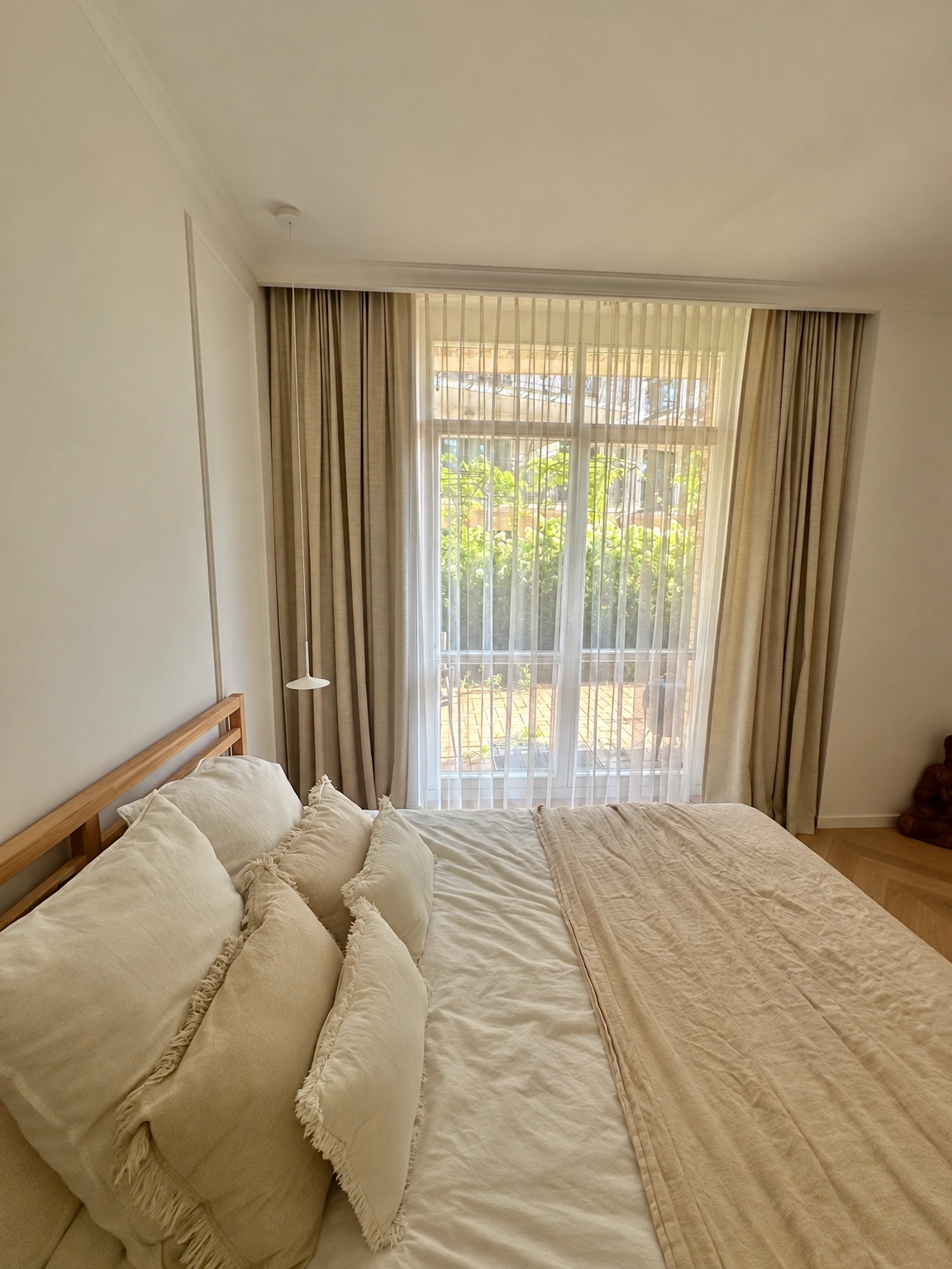 Im Schlafzimmer sind ein Bett mit Kissen und ein großes Fenster mit Vorhängen zu sehen.