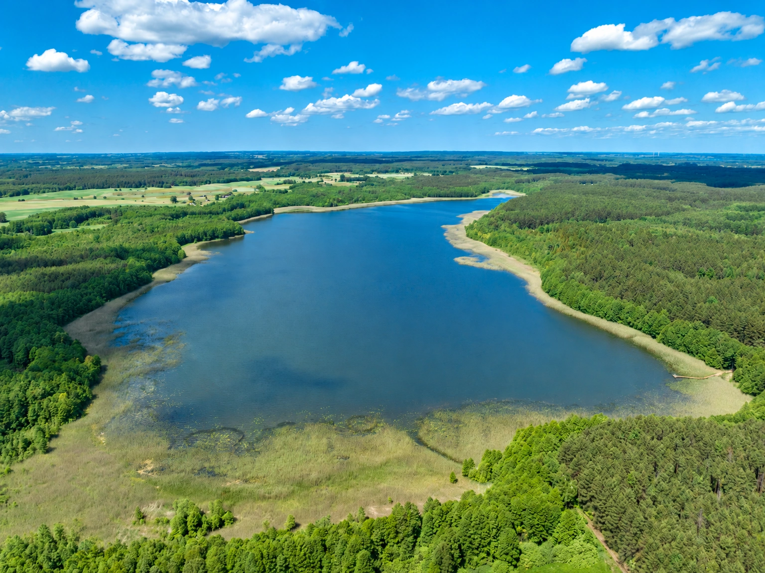 Von oben ist ein See mit gewundenen Ufern zu sehen, der von Wäldern und Wiesen umgeben ist.